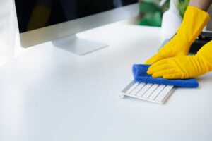 Pessoa limpando a sala, o funcionário da limpeza está usando um pano para limpar o teclado na sala de escritório da empresa. cuidados com a covid