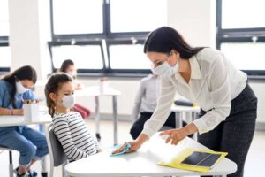 Professor e crianças com máscara facial na escola, desinfetando mesas