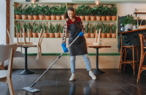mulher sorrindo enquanto faz a limpeza profissional de sua pequena empresa com uma mop