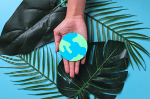 fundo azul com plantas em cima e uma mão segurando uma miniatura do planeta terra
