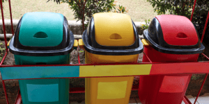 Três latas de lixo multicoloridas para coleta seletiva ao ar livre. As cores de cada caixa indicam o tipo de lixo a ser armazenado.